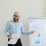 Smiling businessman with beard presenting financial charts at an office meeting.
